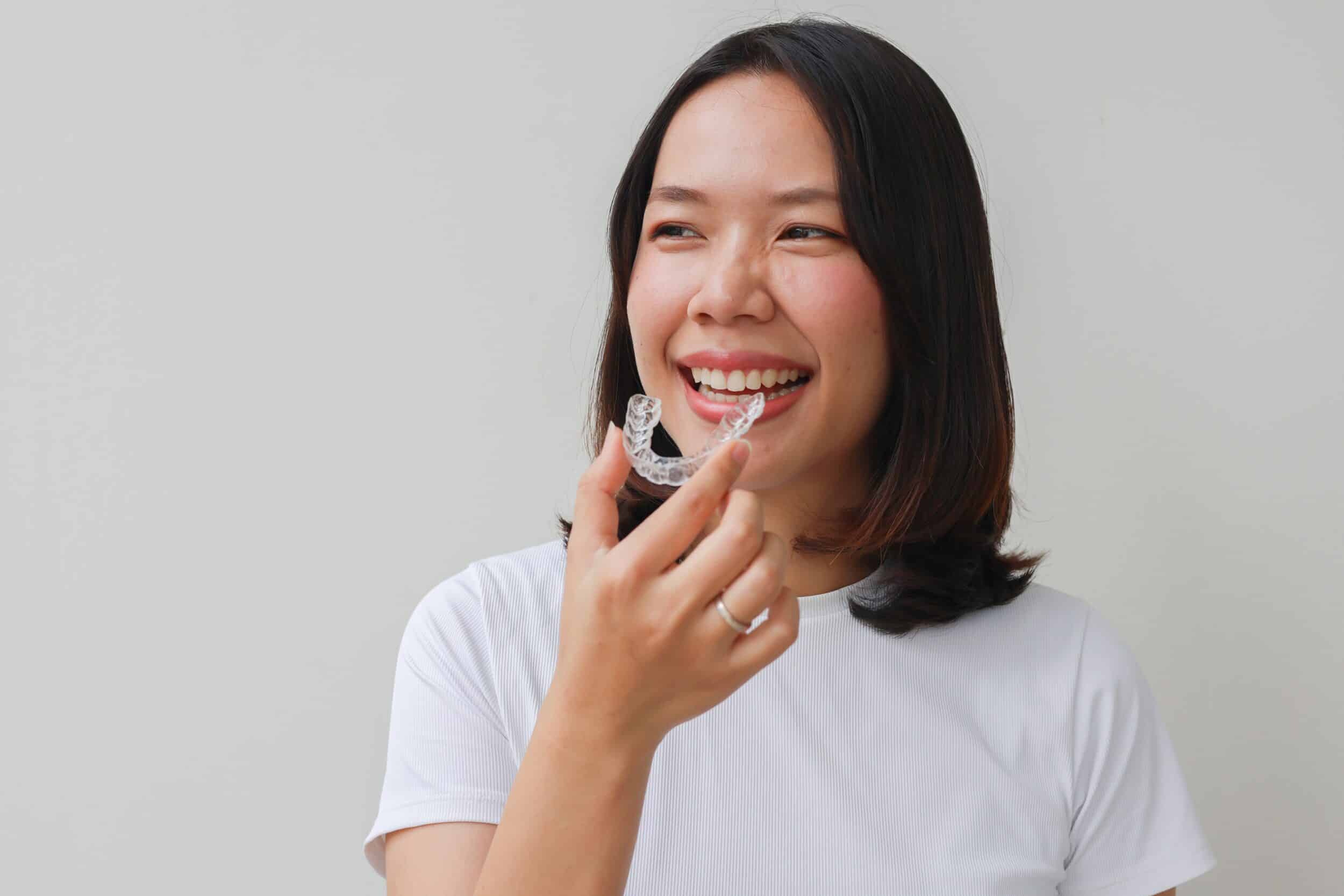A young woman holds a clear dental aligner in her hand, showcasing invisible orthodontic treatment designed for straightening teeth