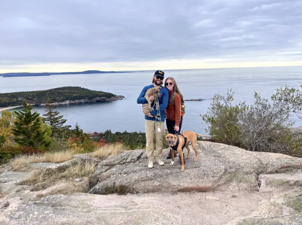 Dr. Sydney Nolan and her husband and their two dogs standing on a rock formation by a lake.